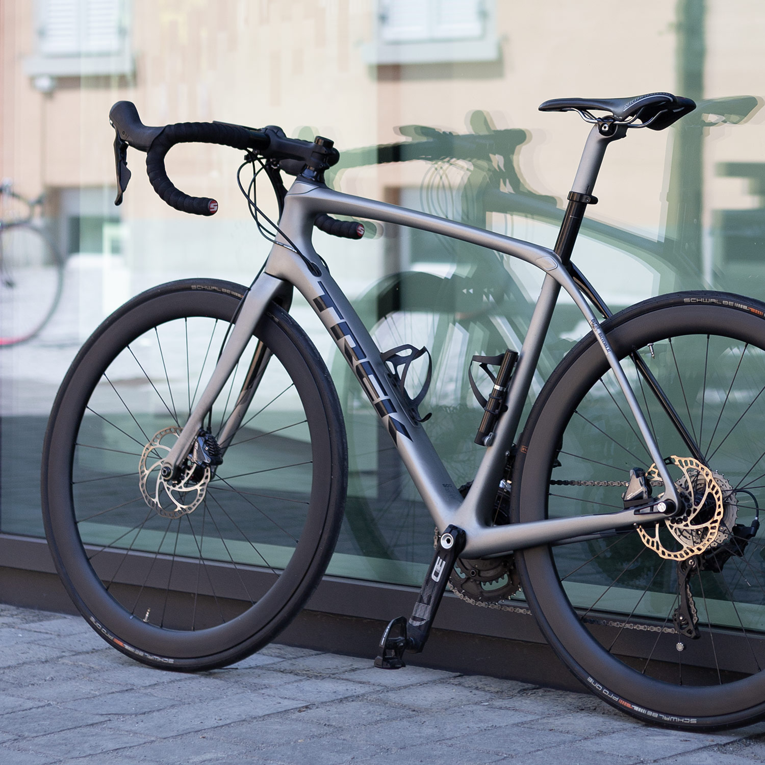 Graues Rennrad mit schwarzen Felgen vor spiegelnder Fensterscheibe